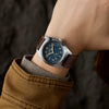 Close-up of a wrist wearing a watch with a brown leather strap and blue dial.