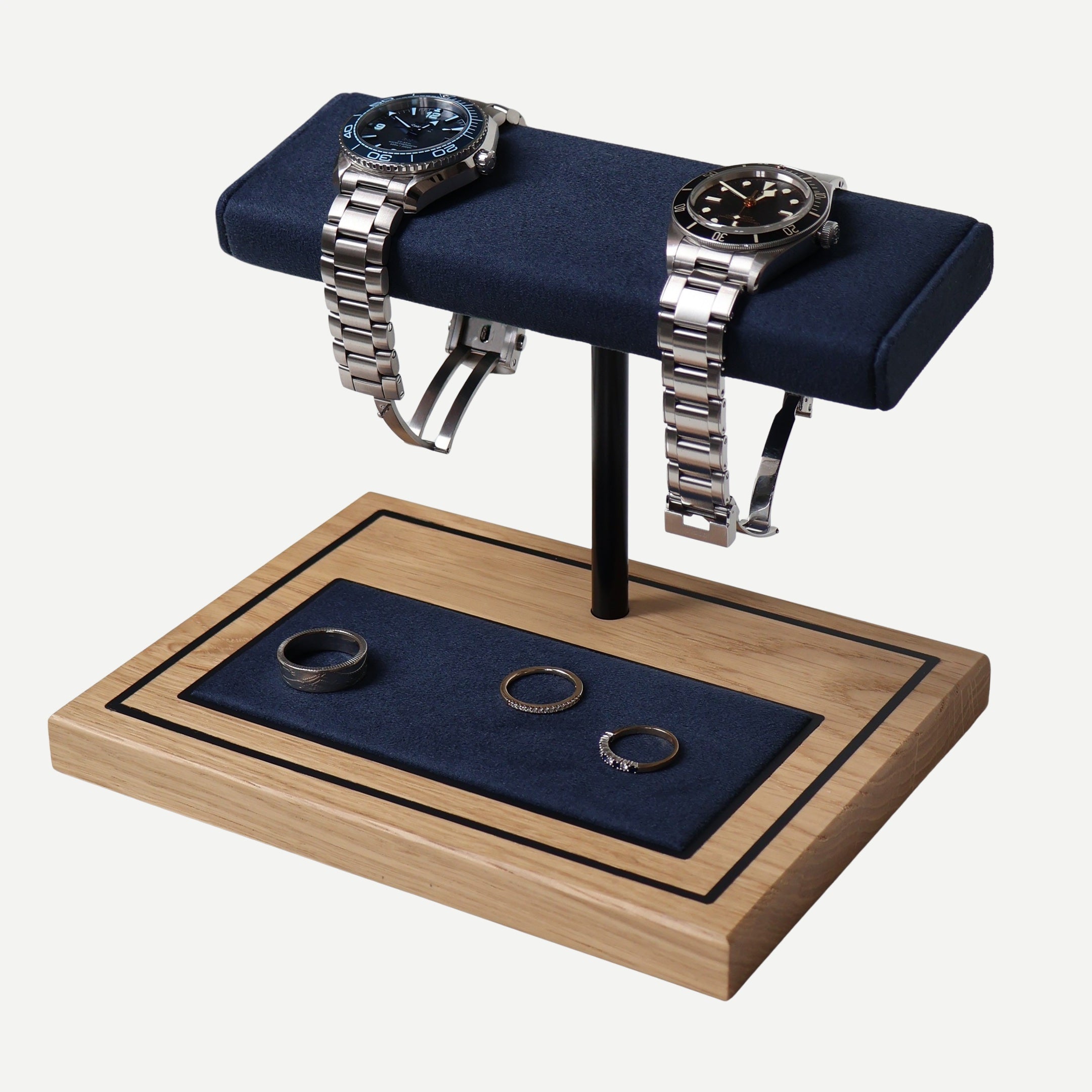 A watch stand with a marine blue cushion on top, made of white oak, displaying watches and rings on its upper and lower pads.